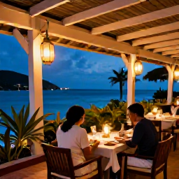 Caribbean Holidays, Antigua August, Elegant beachfront restaurant in Antigua with a couple dining outdoors in the evening, lanterns, sea views and tropical plants