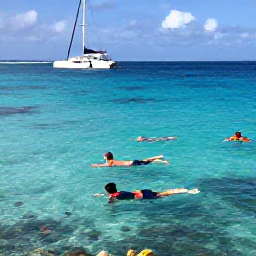 Caribbean Holidays, Aruba Holidays July, Visitors swimming and snorkelling in clear Caribbean water near Aruba, with colourful fish, coral and a catamaran offshore