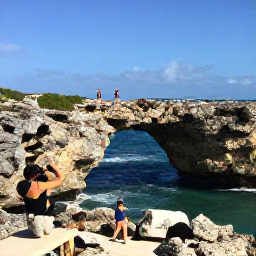 Caribbean Holidays, Aruba Instagram Hotspots, A dramatic view of Aruba's natural rock bridge and rugged coastline under a clear blue sky, with visitors taking photographs from a safe viewpoint