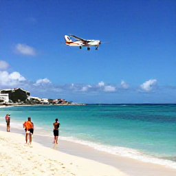 Caribbean Holidays, August Instagram Spots, A sunny panoramic view of Maho Beach in Sint Maarten with a low-flying aeroplane approaching above the shoreline, clear Caribbean water and visitors taking photographs