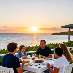 Caribbean Holidays, Bermuda Family Holidays, A family enjoying a relaxed meal on an outdoor terrace overlooking the Bermuda coastline at sunset