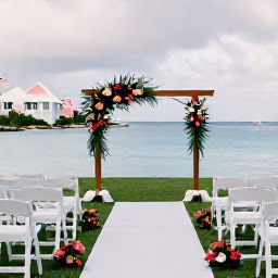 Caribbean Holidays, Bermuda March Weddings, Elegant seaside wedding ceremony in Bermuda in March, with white chairs, tropical flowers, pastel buildings and calm blue sea