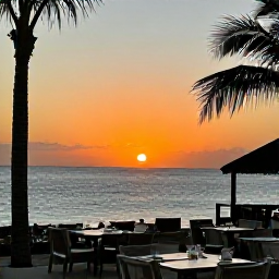 Caribbean Holidays, Cayman Islands March, Cayman Islands sunset viewed from a beachfront restaurant, with glowing sky, palm silhouettes, calm sea and tables prepared for dinner