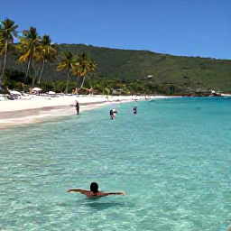 Caribbean Holidays, Cheap November Holidays, Visitors swimming in clear shallow water beside a sandy Guadeloupe beach, with green hills and palm trees in the background