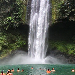 Caribbean Holidays, Dominica Tours, A dramatic Dominica waterfall surrounded by rainforest, with visitors swimming in a natural pool