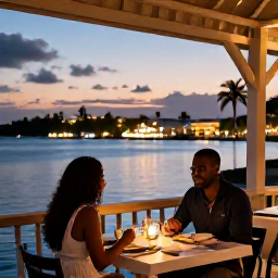Caribbean Holidays, Grenada Honeymoons, A romantic open-air restaurant in St George's, Grenada, with a couple dining at sunset and harbour lights behind them