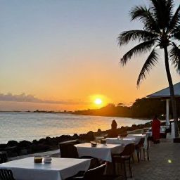 Caribbean Holidays, Guadeloupe January Breaks, Sunset over a lively Guadeloupe waterfront with outdoor tables, palm trees and warm evening light