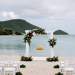 Caribbean Holidays, Guadeloupe Weddings, An elegant beachfront wedding ceremony in Guadeloupe with white chairs, tropical flowers, calm blue water and distant green hills