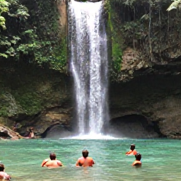 Caribbean Holidays, Jamaica Multi-Country Holidays, Visitors swimming beneath the clear waters of a Jamaican waterfall surrounded by tropical forest and rocks