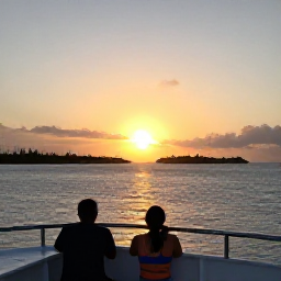 Caribbean Holidays, March Tours, A couple enjoying a sunset cruise off the Turks and Caicos Islands, with a golden sky, calm sea and silhouettes of low islands on the horizon